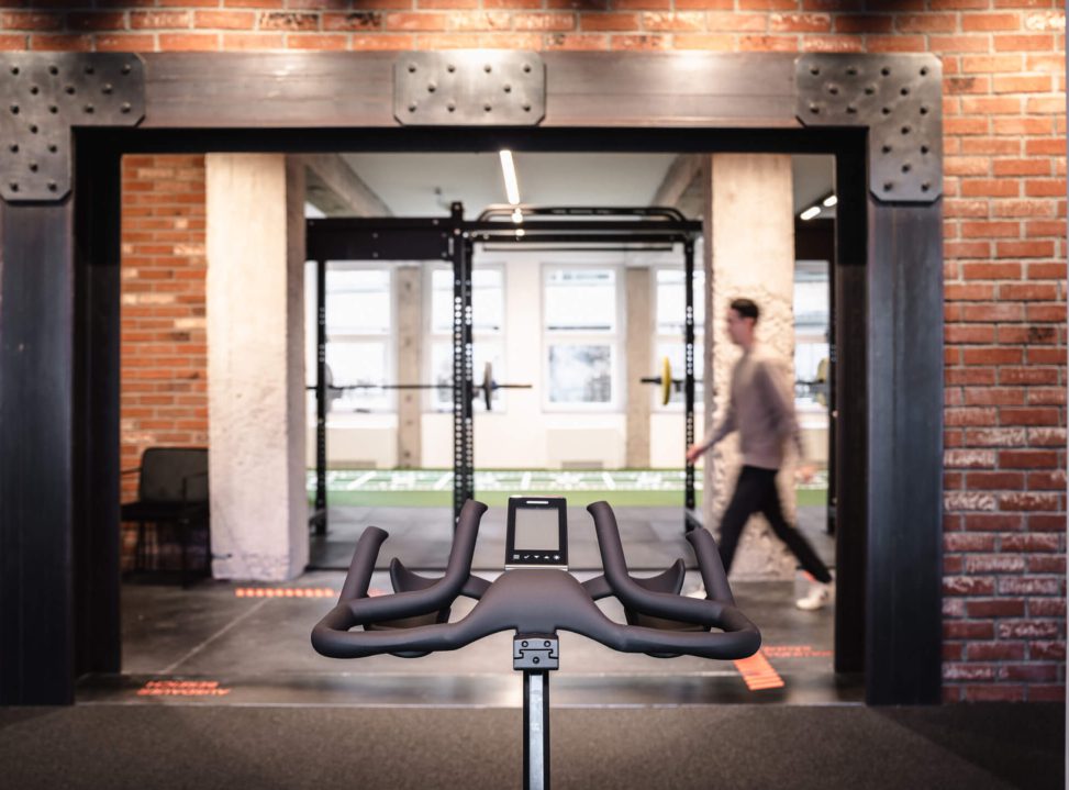 Modernes Fitnessstudio mit Stationärfahrrad und Krafttrainingsbereich im Hintergrund.