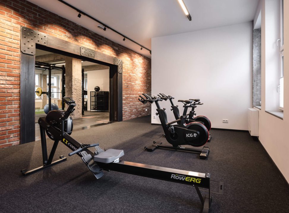 Modernes Fitnessstudio mit Rudergerät und Bikes vor Backsteinwand und hellem Lichtkonzept.