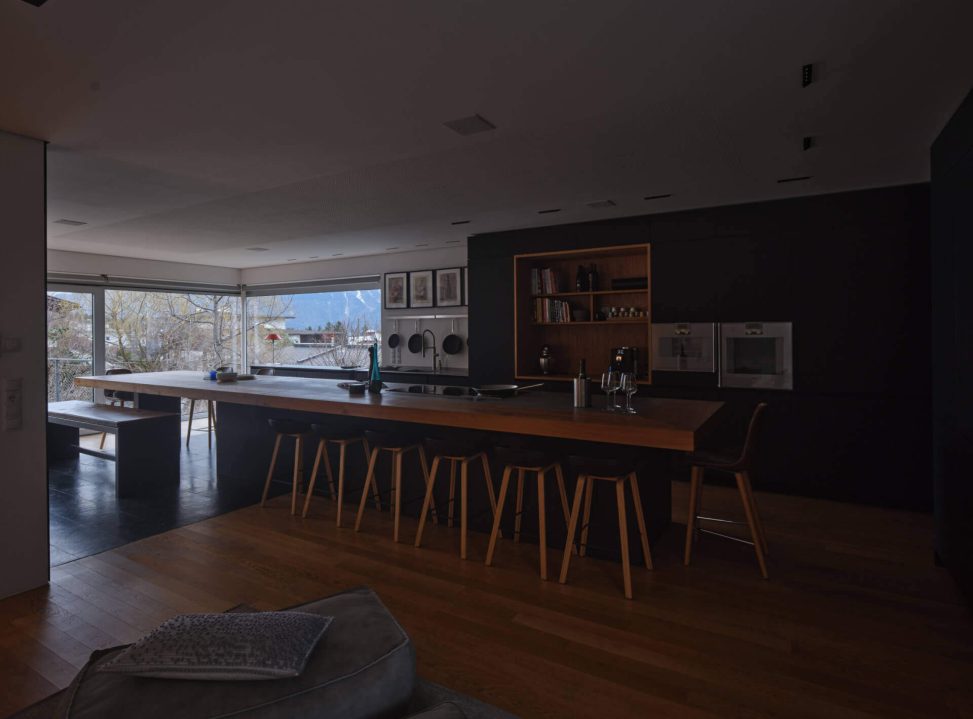 Moderne Küche mit Holztheke, eleganten Stühlen und viel natürlichem Licht durch große Fenster.