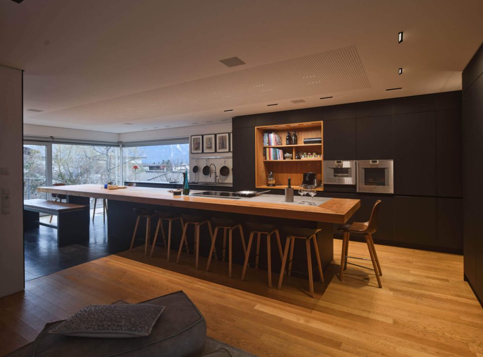 Moderne Küche mit Holz- und Metallakzenten, große Fenster für Tageslicht und stilvolle Beleuchtung.